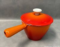 Front view of orange to red gradient enamel cast iron sauce pot with lid and handle.