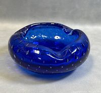 Front angle of deep blue Murano glass ashtray with visible internal air bubble design and ruffled rim with cigarette rests.