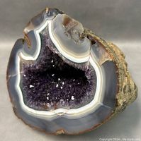 Front view of geode showing deep purple amethyst crystals inside and white-gray agate banding around opening.