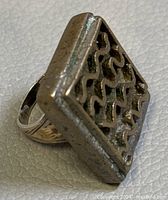 Side angle showing the square top with a raised wavy geometric pattern and visible wear on silver.