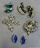 Top view of lot showing brooch and four pairs of earrings with various colored rhinestones on a gray background