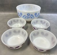 Front angle view of the large blue daisy mixing bowl and four small purple leaf berry bowls arranged in front