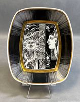 Front view of the rectangular porcelain serving bowl showing the detailed sun and face artwork with gold accents on a black background.