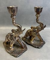 Pair of vintage sterling silver elephant candleholders shown from an angle, highlighting raised trunks holding candle cups and textured bases.