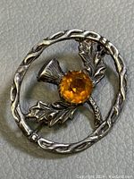 Close-up photo of vintage sterling silver Scottish thistle brooch showing the oval frame and amber faceted crystal center.