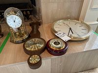 Overview of two barometers, mantle clock under glass dome, and wall clock on a ledge.