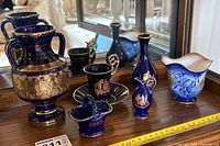 Wide view of all seven pieces of blue and gold ceramic decor arranged in front of mirror.