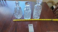 Three crystal decanters displayed side by side on a wooden table with a measuring tape showing about 9-10 inches tall.