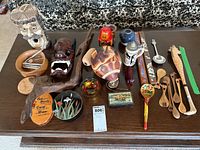 Overall view of various decorative wooden and ceramic figurines and kitchen utensils arranged on a wooden table.