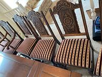 Set of six dining chairs in a row showing carved wooden backs and striped upholstered seats