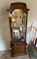 Front view of the wooden display cabinet showing glass shelves filled with various items, with details of the upper arched wood design and two drawers below.