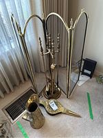 Full view of brass fireplace tool set on round stand with fire screen behind, brass pitcher and bellows on floor.