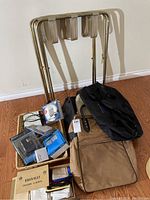 Photo showing two metal luggage racks with beige fabric straps along with multiple duffel bags and packaged electronics.