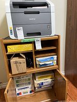 Full view of printer on wood cabinet with paper boxes inside cabinet