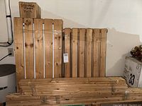 Wide view of multiple large wooden slats and smaller bundled slats against the wall, with a box of bolts on top.