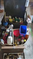Open metal toolbox containing multiple small bottles, tubes of silicone and adhesive, spray cans and plastic containers organizing various items.