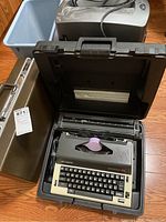 Olympia typewriter in black hard carrying case with briefcase and paper shredder in background