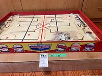 Full top view of a vintage electric table hockey game showing painted rink, red wooden sides with classic NHL team logos, and metal rods controlling player positions.