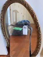 Oval mirror with ornate gold-tone carved frame leaning against wall, reflecting hallway interior and trash bags.