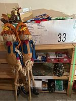 Shelf with large boxed artificial Christmas tree labeled Canterbury Pine and assorted decorations including two scarecrow dolls and Christmas fabric pieces