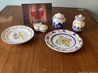 Photo of assortment of five vintage ceramic dishes including two decorative plates, two lidded jars, and a small trinket dish arranged on wooden surface.
