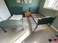 Photo of two single blue beds with curved slatted headboards and footboards, placed side by side in a room with green walls and beige carpet.