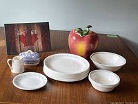 Full set displayed on table including apple cookie jar, plates, bowls, small pitcher, and covered dish. Includes lot number card.