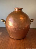 Front view of large hammered copper vase with rounded shape and brass handles visible