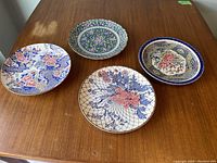 Four decorative vintage Japanese plates arranged on a wooden table showing multiple floral pattern styles.