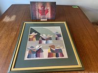 Frontal view of framed petit point showing Peruvian women in colorful traditional dress, with a green matte and gold frame, on a wooden surface with lot sign