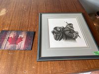 View of framed numbered print showing a man and child in detailed black and white art on wood table.