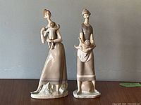 Front view of both figurines side by side on wood table against grey wall