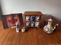 Front view of the wooden spice rack with six ceramic drawers and three decorative ceramic items on a wooden table