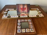 View of large rectangular mirror with five metal coat hooks and ceramic tile decorations, alongside a small square mirror framed with floral ceramic tiles on a wooden surface.