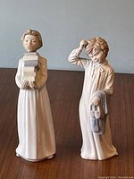 Front view of two Lladro Boys Bedtime porcelain figurines, one glazed holding books, the other matte holding slippers and cloth.