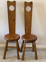 Front view of two antique wooden spinning chairs with tall backs and circular cutouts near top.