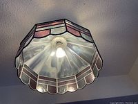 Underside view showing cream-colored tinted and scalloped stained glass panels with a light bulb turned on.