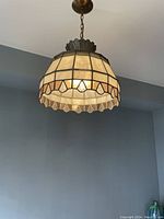 Dome-shaped stained glass ceiling light fixture hanging from a bronze-toned chain with tans and cream colored glass panels and decorative clear teardrop textured glass pieces.