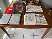 Photo showing five stamp albums on a table, with some albums open revealing pages filled with assorted postage stamps.