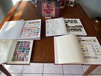 Four open stamp albums displaying various postage stamps on a wooden table with a lot sign in the background.