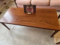 Angled photo of teak coffee table showing wood grain and small scratch on surface.