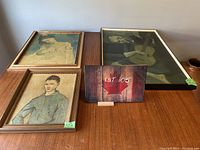 Three framed prints arranged on wood surface: Picasso print of mother and child, a portrait of man in blue shirt, and a print of seated man playing guitar.