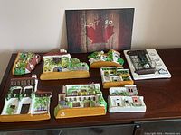 Nine vintage European-style country home wall plaques arranged on a table showing various designs and colors