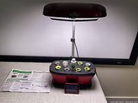 Full photo of the Aerogarden Bounty hydroponic system showing red base with six grow pod slots, adjustable light hood extended, instruction manual, nutrient bottle, and grow pods.