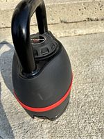 Full view of adjustable kettlebell on concrete surface showing overall shape and condition
