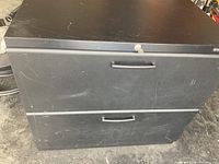 Front view of black metal filing cabinet with 2 drawers and lock on top drawer showing scratches.