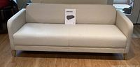 Front view of ivory fabric sofa with clean surface and IKEA LINANAS manual/card on seat