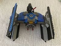 Front close-up of Lego Star Wars Tie Fighter with pilot minifigure standing on top holding red lightsaber