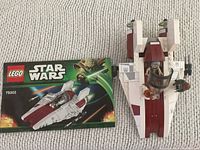 Top view of assembled Lego Star Wars A-Wing Starfighter alongside the original instruction manual, showing details of the model and 3 included Star Wars minifigures.