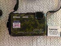 Front view of Nikon Coolpix AW110 camouflage digital camera showing waterproof and shockproof specs, with one Turpow EN-EL12 battery beside it.